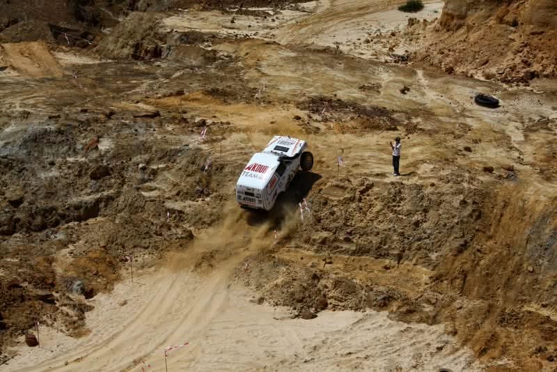 Viewed from above, Wissam Akoury's Niva climbing a steep dirt slope with dust trailing behind it, while a spectator watches from the side of the course.