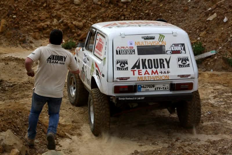 Wissam Akoury's Niva on a rocky off-road course, with a man running alongside it.