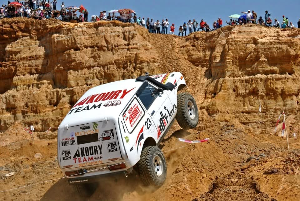 Wissam Akoury's Niva, bearing competition number 23, climbing a steep, rocky dirt slope during an off-road event, with spectators watching from the ridge above.