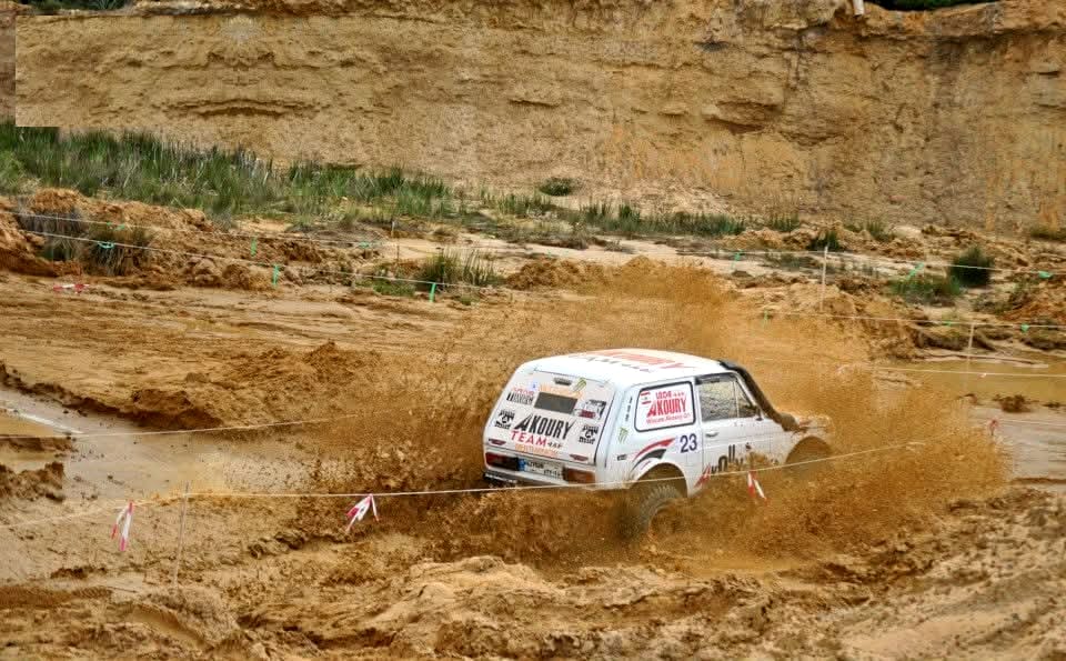 Wissam Akoury's Niva, carrying competition number 23, driving through a flooded section of the off-road course and sending muddy water spraying into the air.
