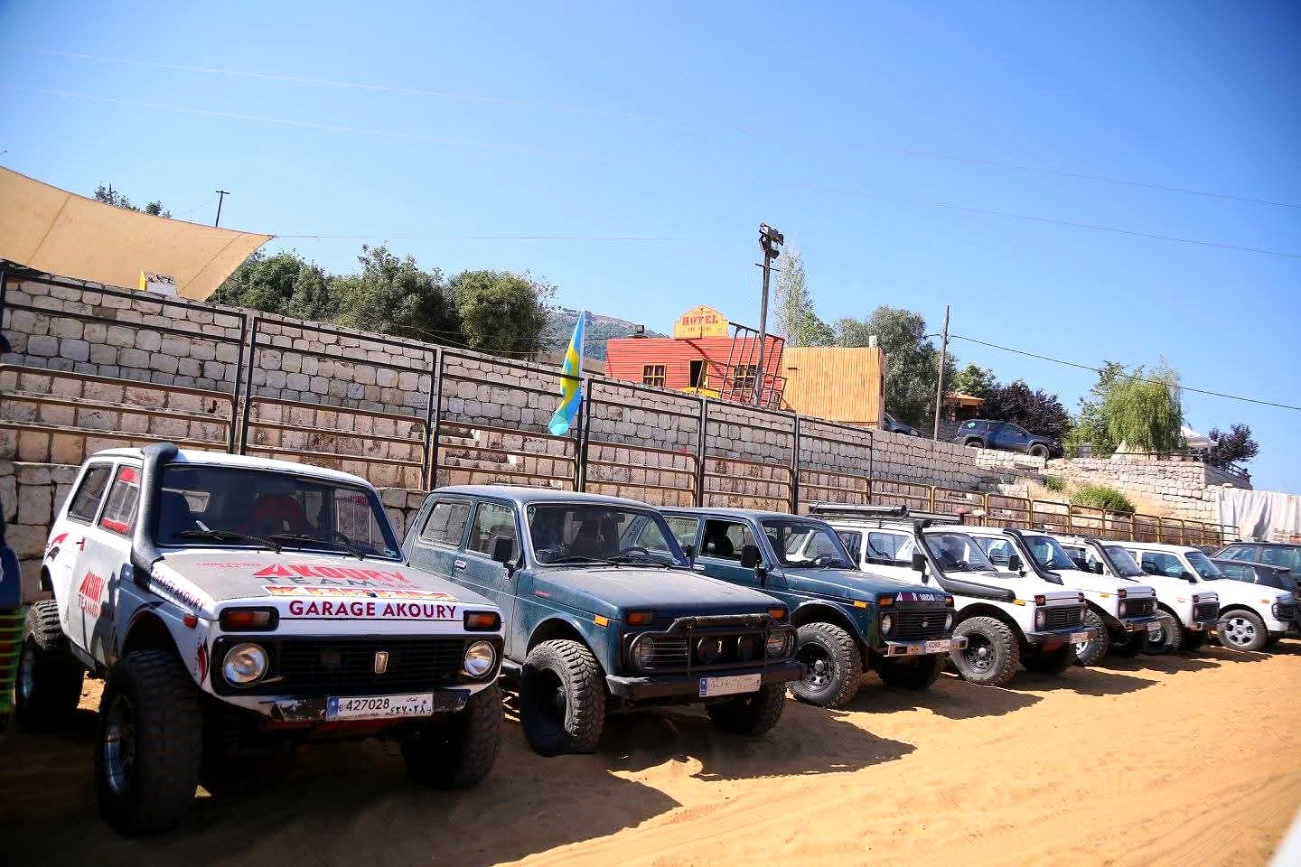 Wissam Akoury's Lada Niva at the front of a lineup of Nivas parked on sandy ground, with several other vehicles lined up behind it.
